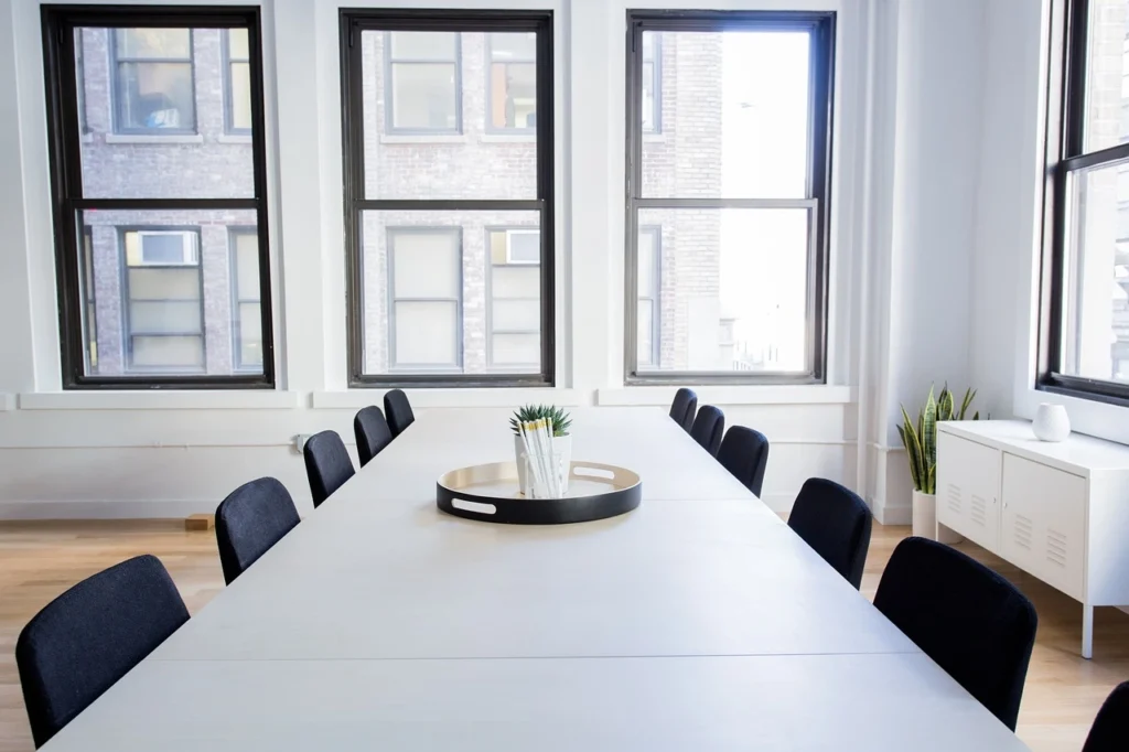 A conference table with black chairs positioned in front of large windows, allowing natural light to illuminate the space.