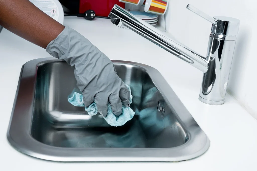 A person wearing a rubber glove scrubs a kitchen sink, ensuring cleanliness and hygiene in the home.