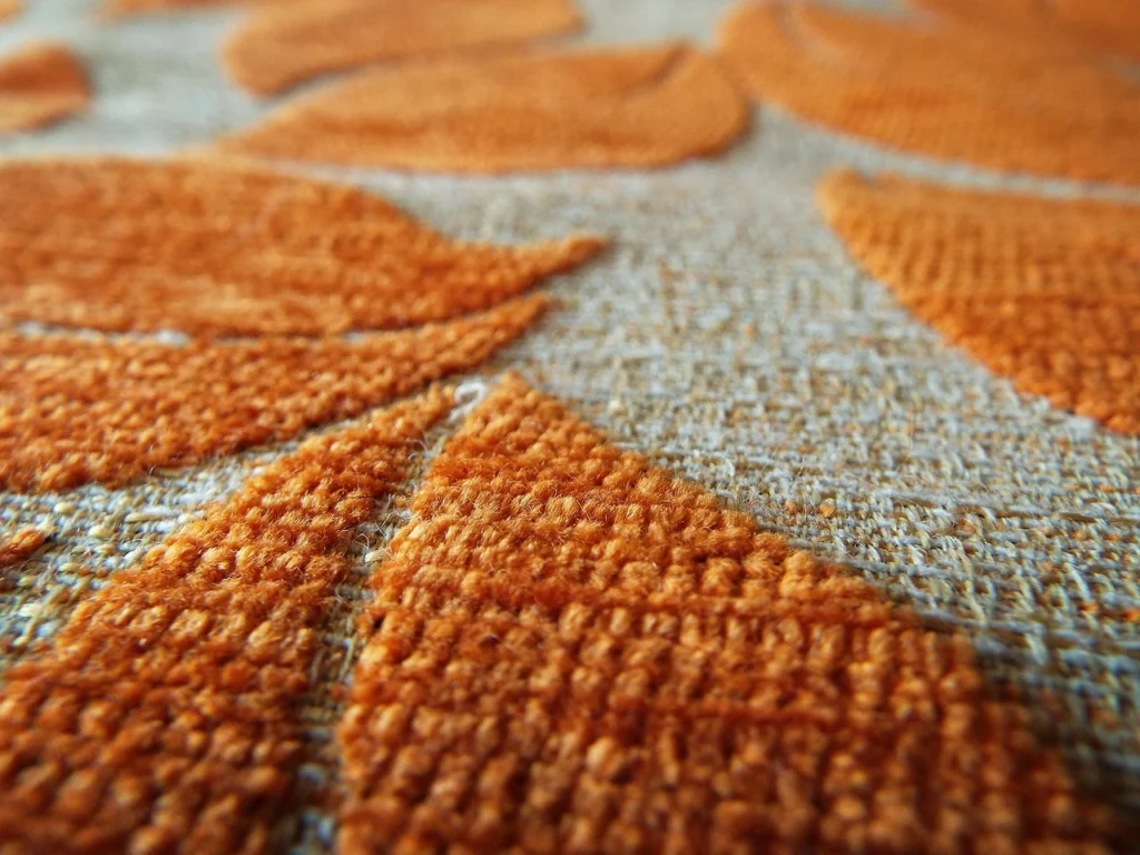 Close-up of orange and gray fabric featuring a leaf pattern, showcasing intricate details and vibrant colors.