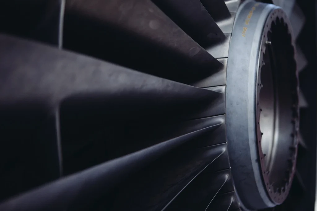 A detailed close-up of dark metal fan blades arranged in a circular pattern, likely from an industrial ventilator or turbine, showcasing the geometric precision and mechanical structure